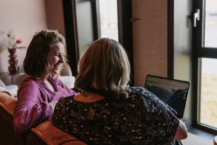 Ryanne overlegt met een klant op de bank over digitale toegankelijkheid, kijkend naar een laptop