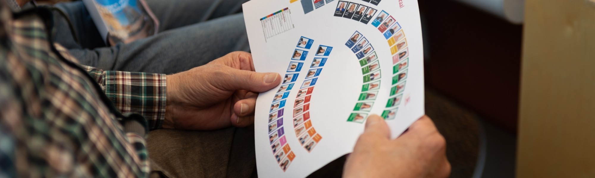Een toeschouwer op de publieke tribune bekijkt een plattegrond van de raadzaal